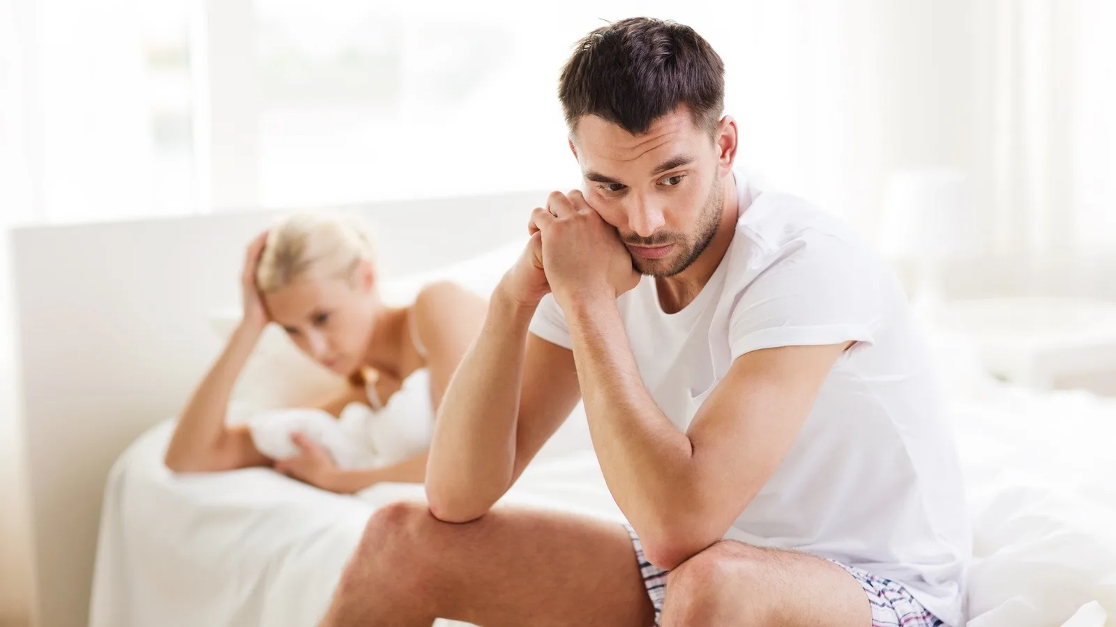 Paar sitzt auf Bett, beide angewandt, symbolisiert Partnerschaftsprobleme