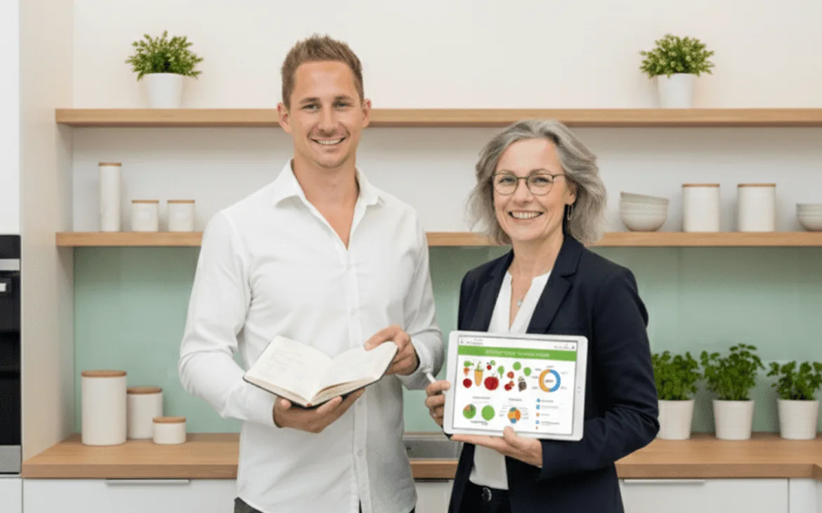 Patrick und Joanne in moderner Küche mit Buch und Tablet, Regale mit Pflanzen im Hintergrund