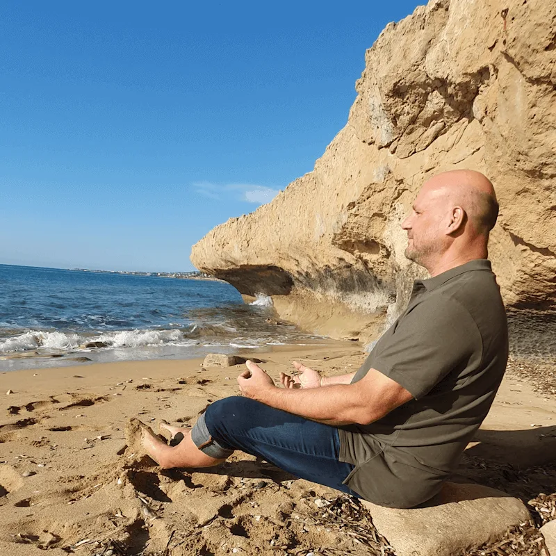Der neue HerzMensch – Videokurs zur Herzverbindung von Jens Tell 5 Jens Tell in olivfarbenem Hemd meditierend am Strand vor Felsen und Meer