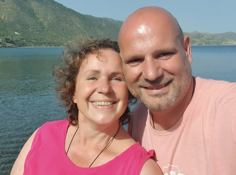 Der neue HerzMensch – Videokurs zur Herzverbindung von Jens Tell 3 Jens Tell und Frau Bianka zusammen lächelnd vor türkisem Meer mit Berglandschaft