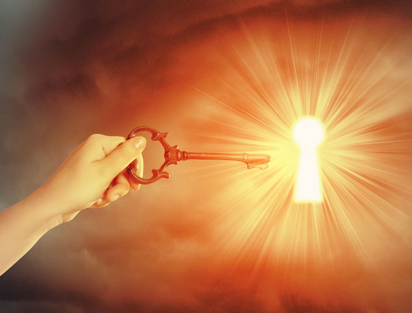 Hand hält goldenen Schlüssel vor Lichtstrahl und Himmel