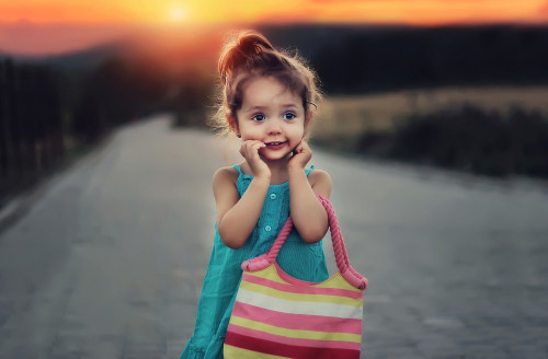 Kleines Mädchen in buntem Outfit mit rosa Rucksack bei Sonnenuntergang
