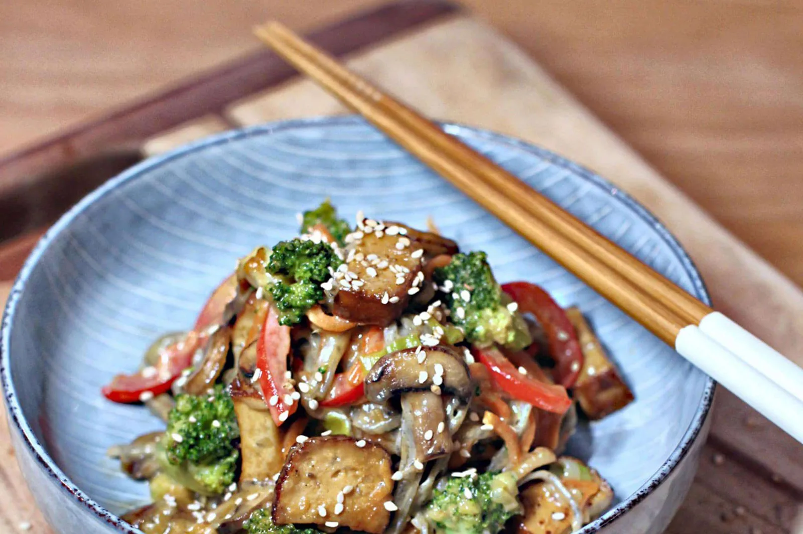 Asiatisches Gericht mit Tofu, Brokkoli und Sesamkörnern auf blauem Teller mit Stäbchen
