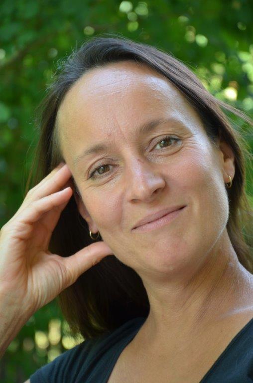 Frau mit braunem Haar vor grünem Laub, Porträtfoto
