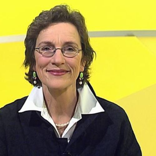 Porträt einer Frau mit dunklem Haar, Brille und Ohrringen vor gelbem Hintergrund
