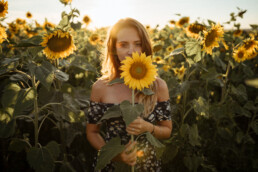Frau mit rötlichem Haar hält Sonnenblumen in Sonnenblumenfeld