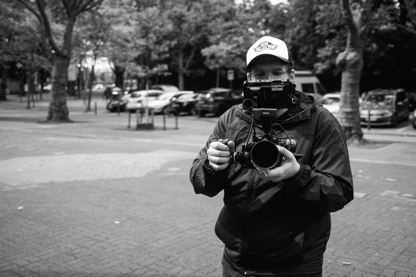 Dominik Garban hält Sony-Videokamera in urbaner Parkanlage, Schwarz-Weiß-Porträt