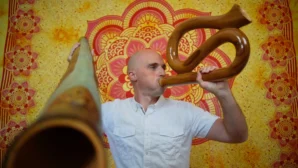 Mann spielt Didgeridoo vor rot-gelbem Mandala-Hintergrund, Didgeridoo Kurs für Anfänger