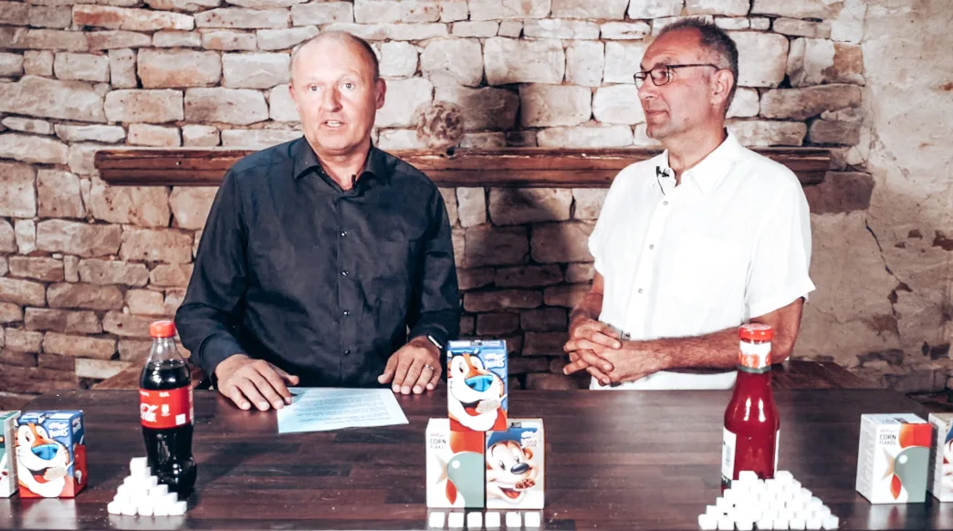 Zwei Männer diskutieren am Tisch mit Zuckerprodukten und Süßgetränken