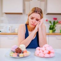 Frau in Küche vor zwei Tellern mit Desserts, eine Hand am Hals, zögernd schauend