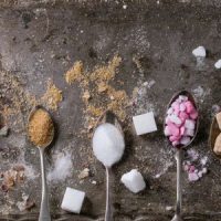 Zutaten auf grauem Untergrund: Löffel mit Zimt und Zucker, weiße Würfel, rosa Blüten
