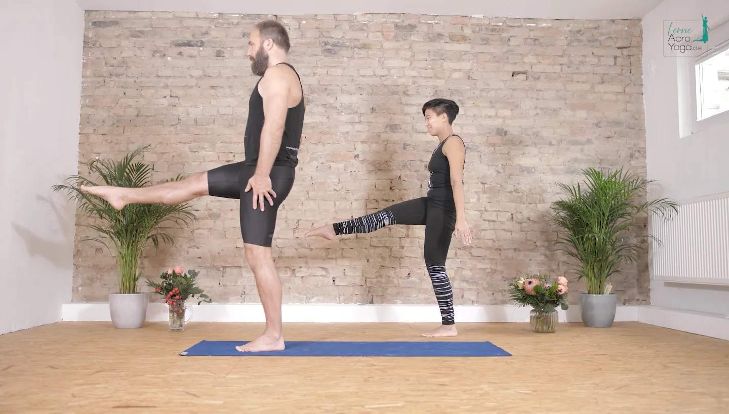 Die AcroYoga Uni – Mit Spiel & Spaß AcroYoga lernen 15 Mann und Frau führen AcroYoga-Übung im Studio auf, Mann im Einbeinstand
