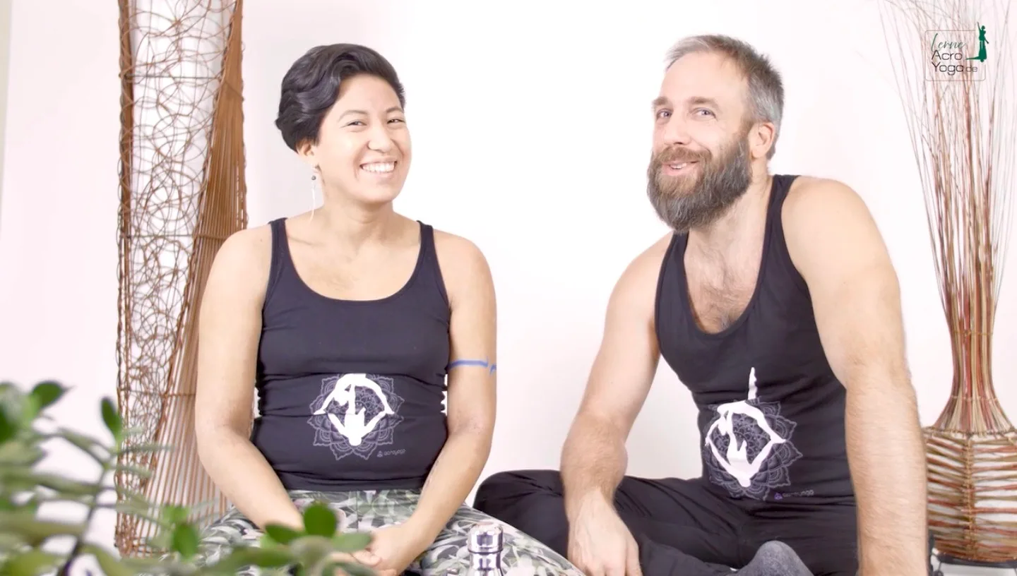 Die AcroYoga Uni – Mit Spiel & Spaß AcroYoga lernen 7 Zwei Menschen in schwarzen Yoga-Tops sitzen auf Kissen vor weißem Hintergrund