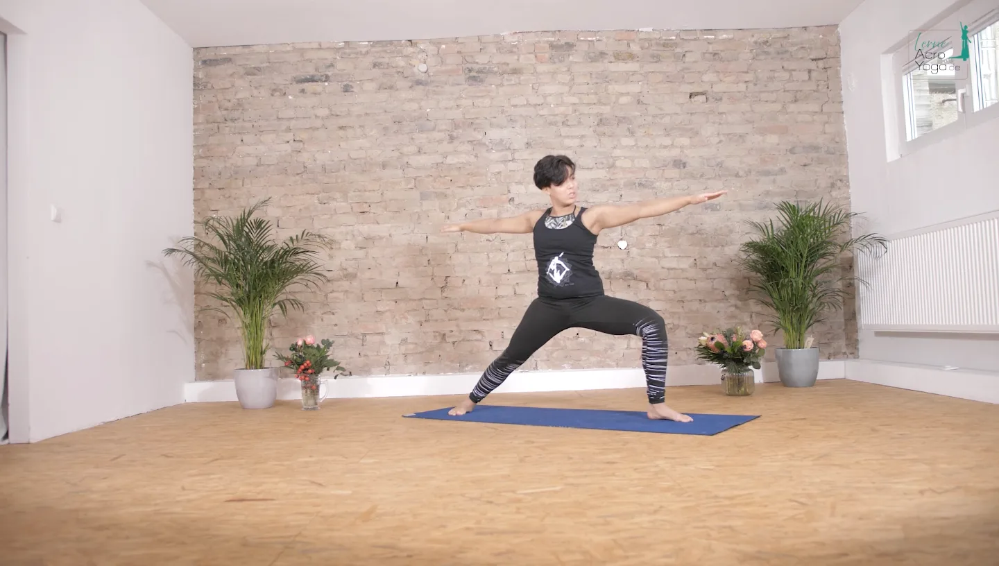 Die AcroYoga Uni – Mit Spiel & Spaß AcroYoga lernen 9 Frau in schwarzem Yoga-Top und gestreifter Leggings in Warrior-Pose auf blauer Matte