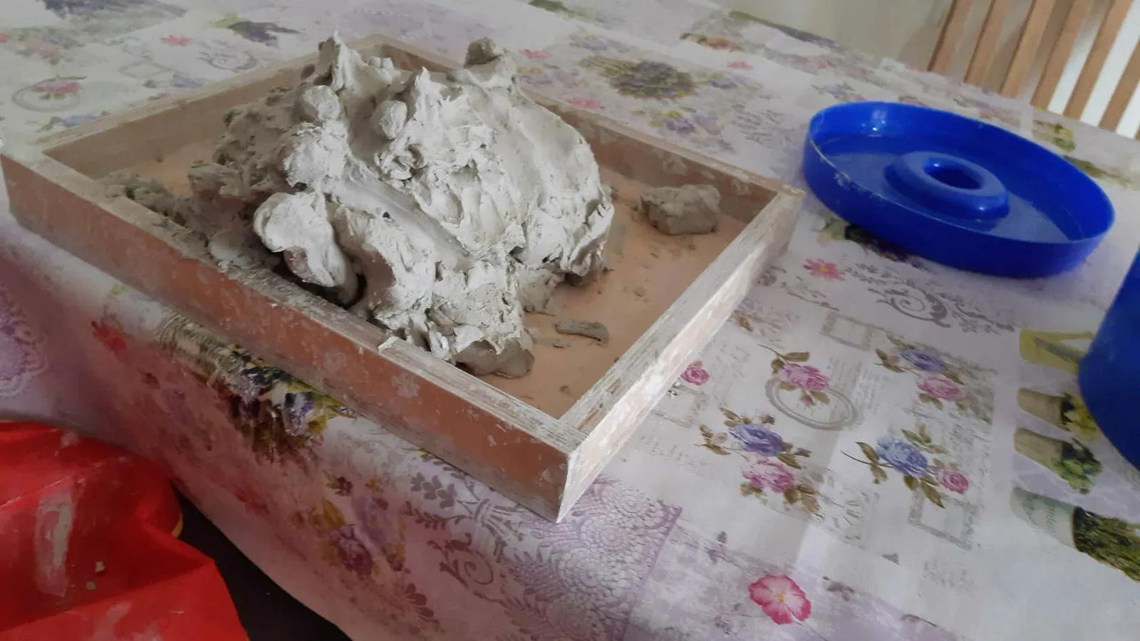 Tonfeld mit Tonmasse in Holzrahmen, blaue Schale daneben auf gemustertem Tuch