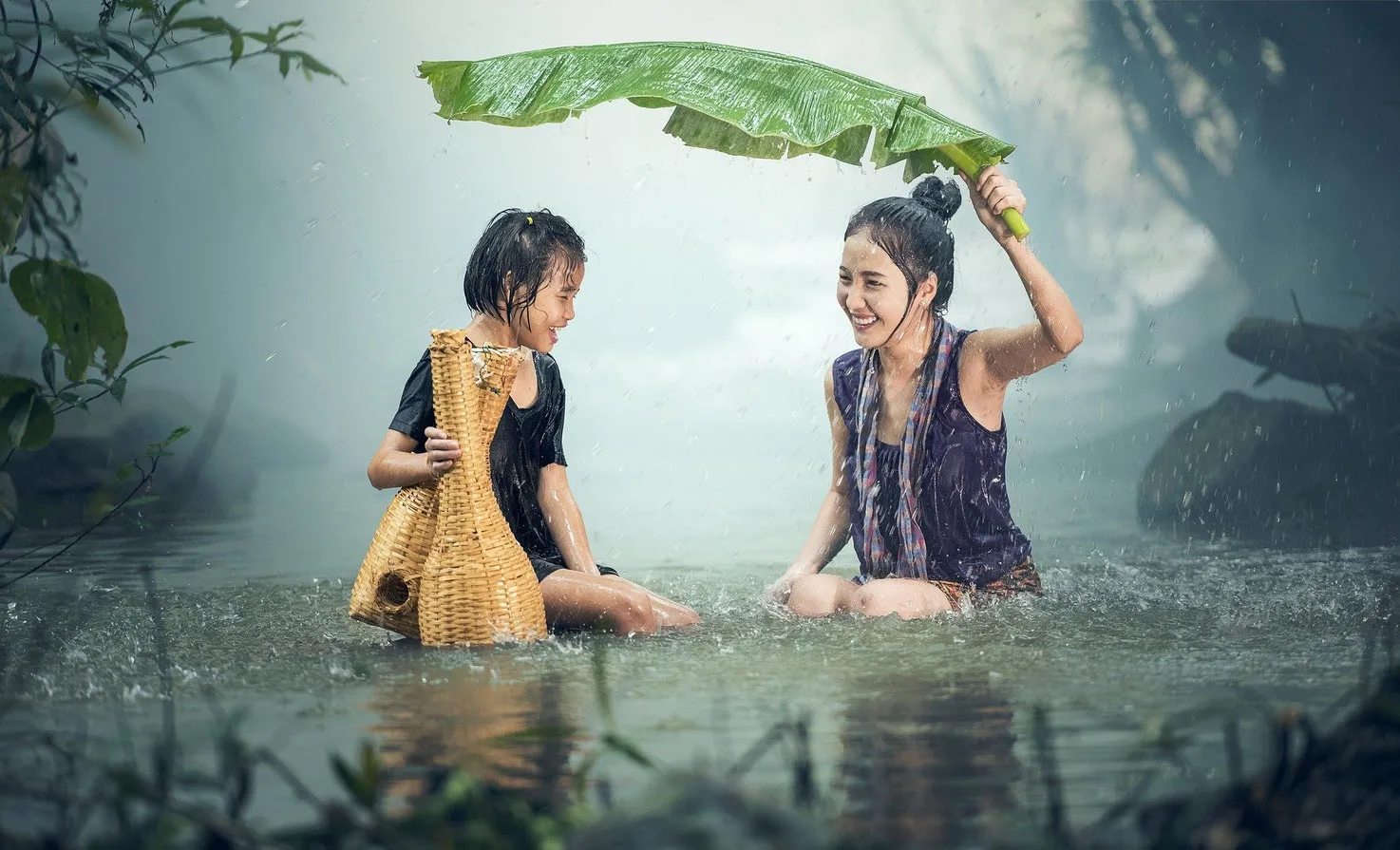 Zwei Mädchen spielen im Regen mit Blattschirm im Wasser