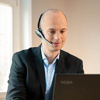 Die perfekte Altersvorsorgeberatung – Videokurs für Finanzberater 11 Robert Peukert mit Headset am Laptop, dunkler Anzug, hellblaues Hemd, telefoniert