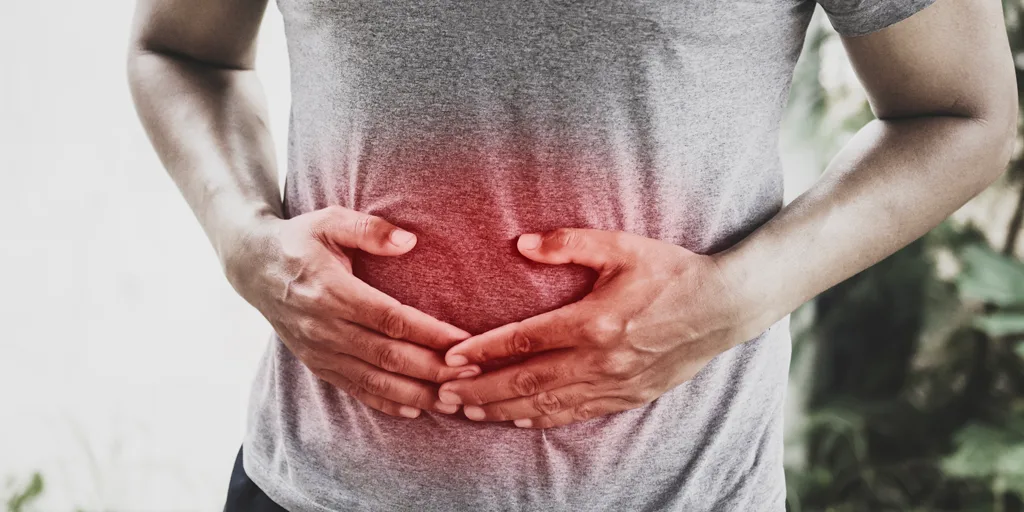 Mann in grauem T-Shirt hält sich den Bauch, rote Schmerzzone im Magen-Darmbereich hervorgehoben