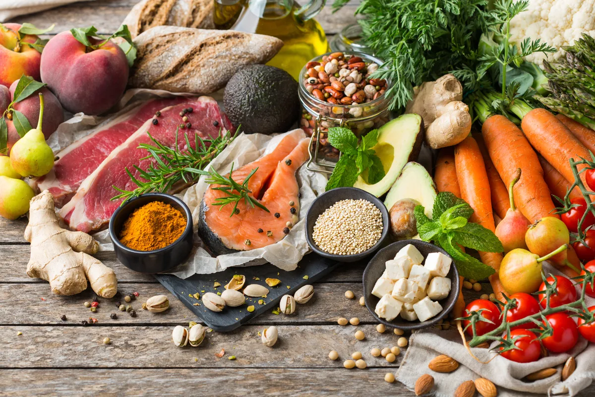 Flat-Lay Arrangement mit Obst, Gemüse, Getreide, Nüssen, Fisch und Gewürzen auf Holzuntergrund