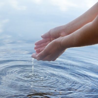 Die Sprache des Wassers – Live-Workshop zu Wasserqualität 2 Hände halten Wasser über Meer mit Wellenmuster, Symbolbild für Die Sprache des Wassers