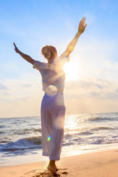 Die Sprache des Wassers – Live-Workshop zu Wasserqualität 4 Frau mit erhobenen Armen im Sonnenaufgang am Strand, abnehmen und vital fühlen