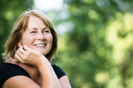 Porträt einer lächelnden Frau mit blondem Haar vor grünem Naturhintergrund