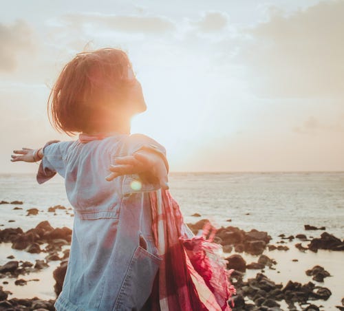 Frau am Strand bei Sonnenuntergang mit ausgebreiteten Armen, Jeansjacke und rotem Tuch
