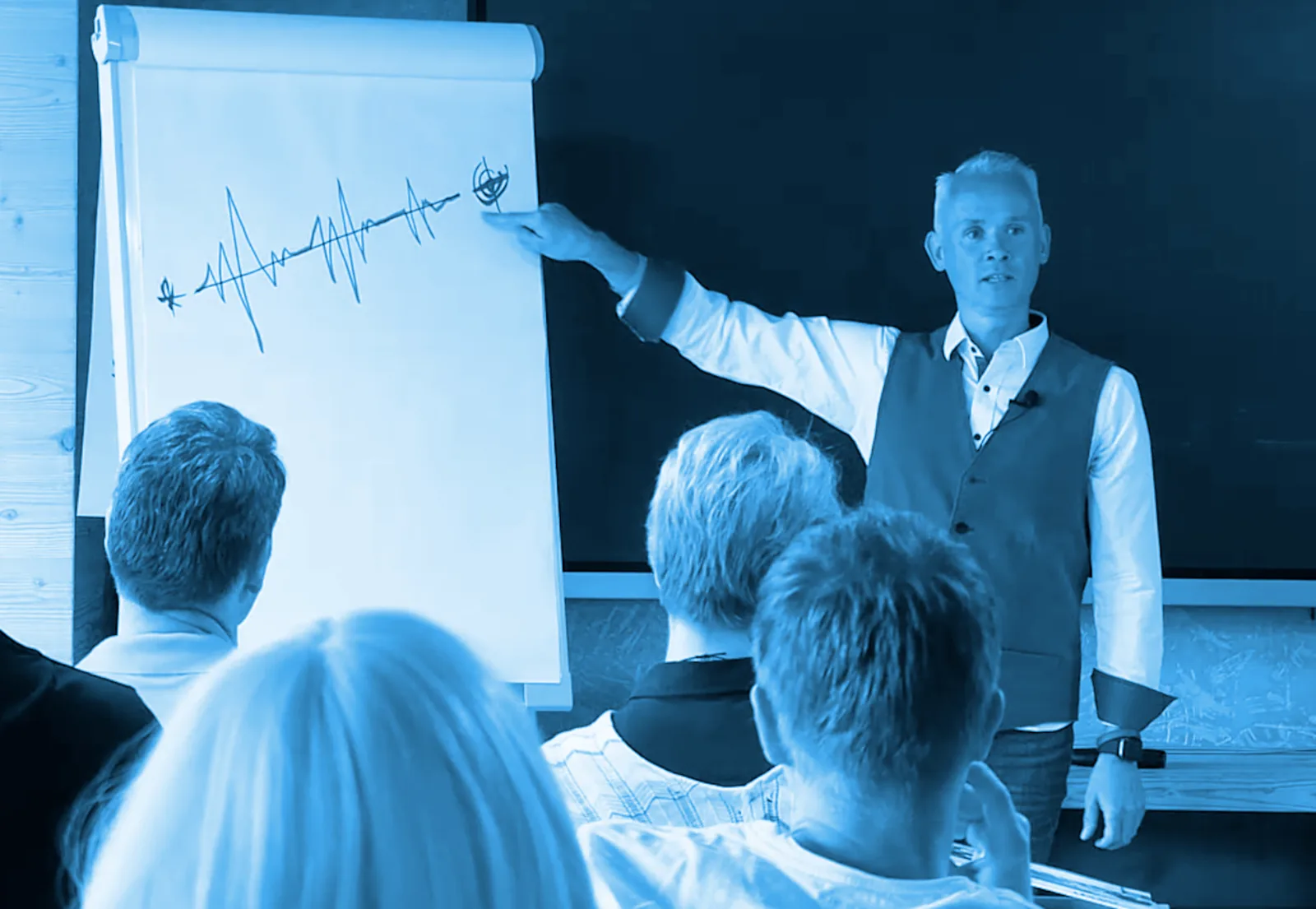 Andreas Damon präsentiert Flipchart mit Verlaufsgrafik vor Publikum in Seminarraum