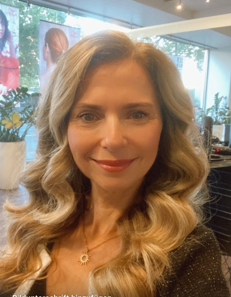 Portrait: Peggy Stapel, Frau mit blondem welligem Haar, Halskette, helles Interieur