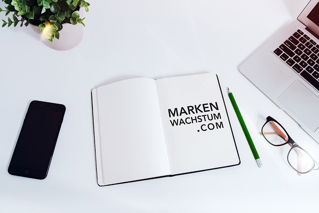 Arbeitsplatz mit Notizbuch mit Markenwachstum.com Logo, Laptop, Smartphone und Brille auf weißem Schreibtisch