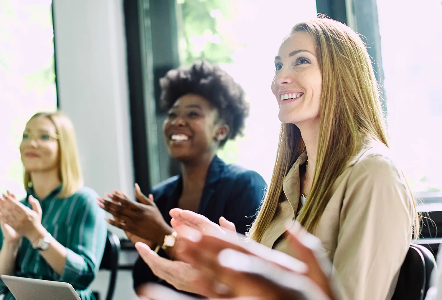 Drei lachende Frauen unterschiedlicher Herkunft applaudieren zusammen in Workshop-Setting