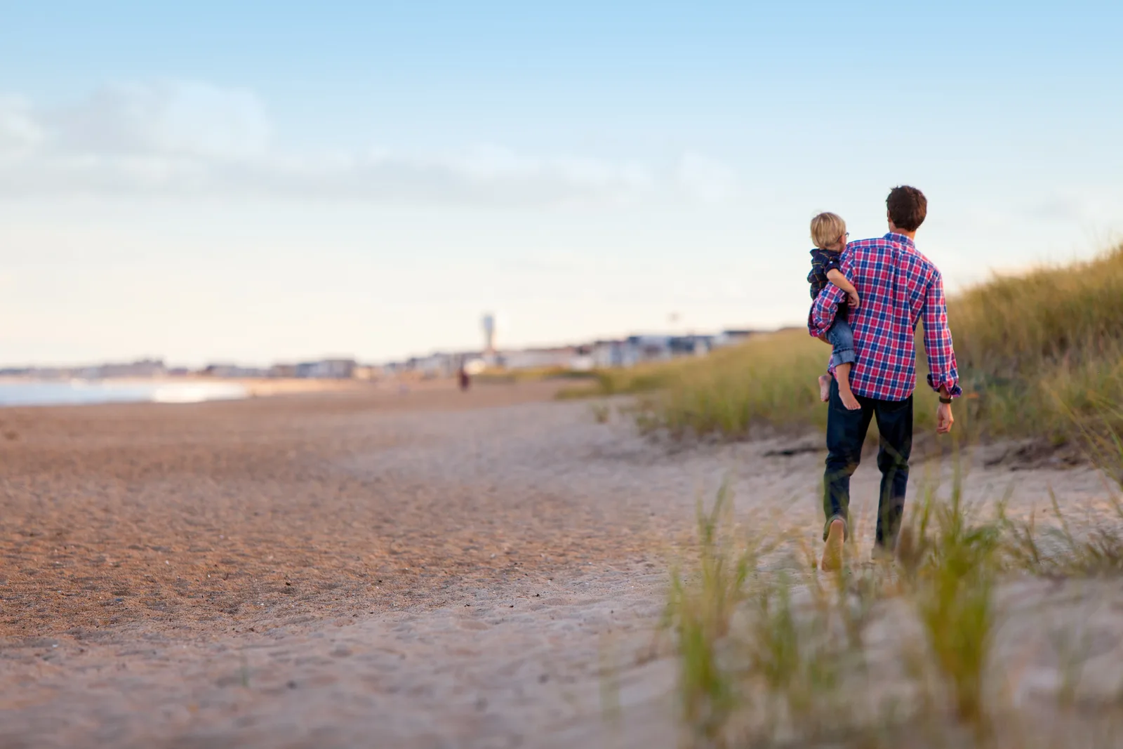 Mann mit Kind auf der Schulter am Strand, blickt aufs Meer hinaus
