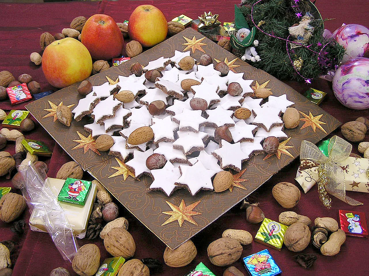Zimtsterne Gebäck mit weißer Glasur auf brauner Platte mit Walnüssen und Weihnachtsdekoration