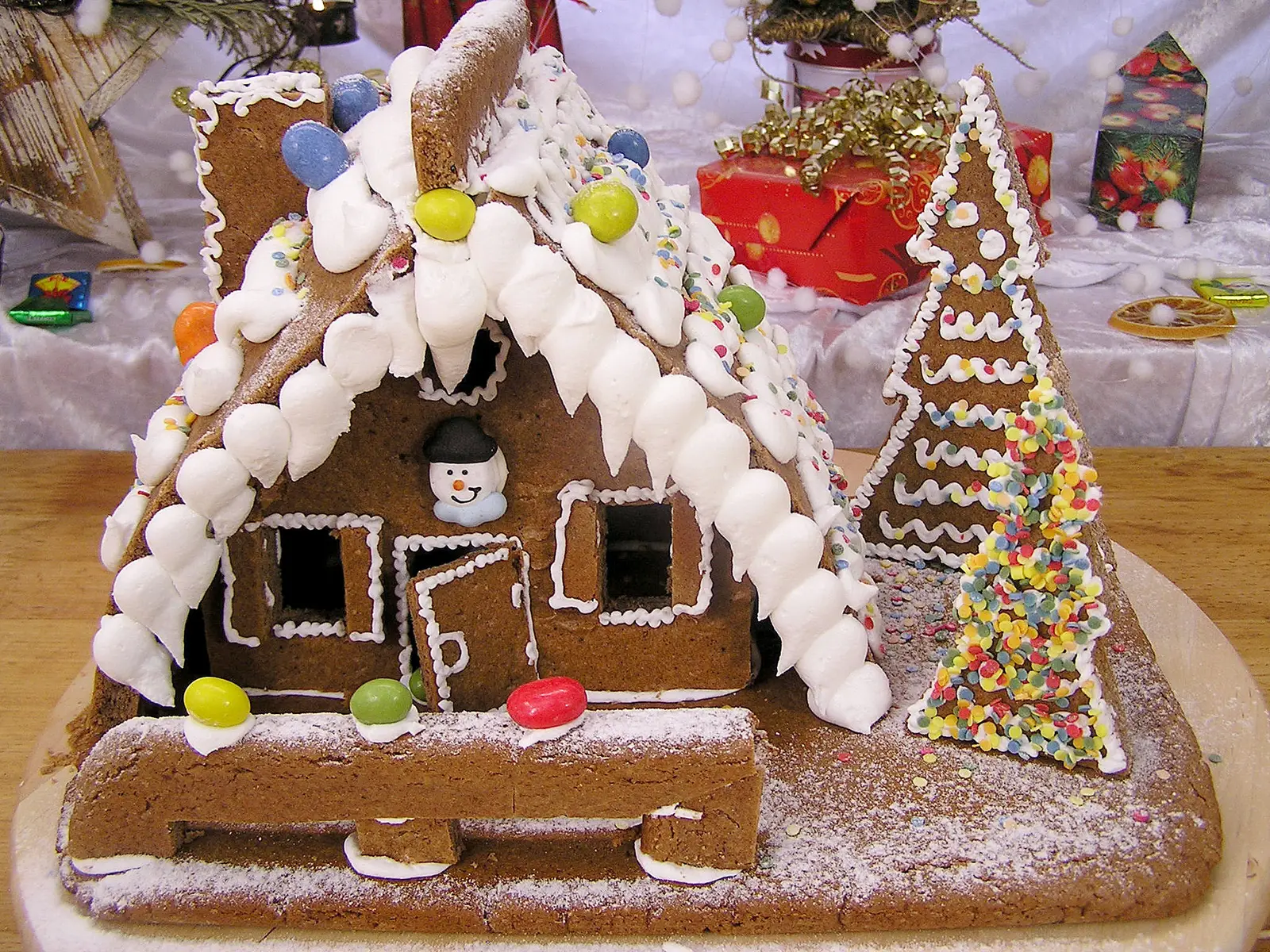 Lebkuchenhaus mit weißem Zuckerguss-Dach, Weihnachtsbaum und farbiger Dekoration