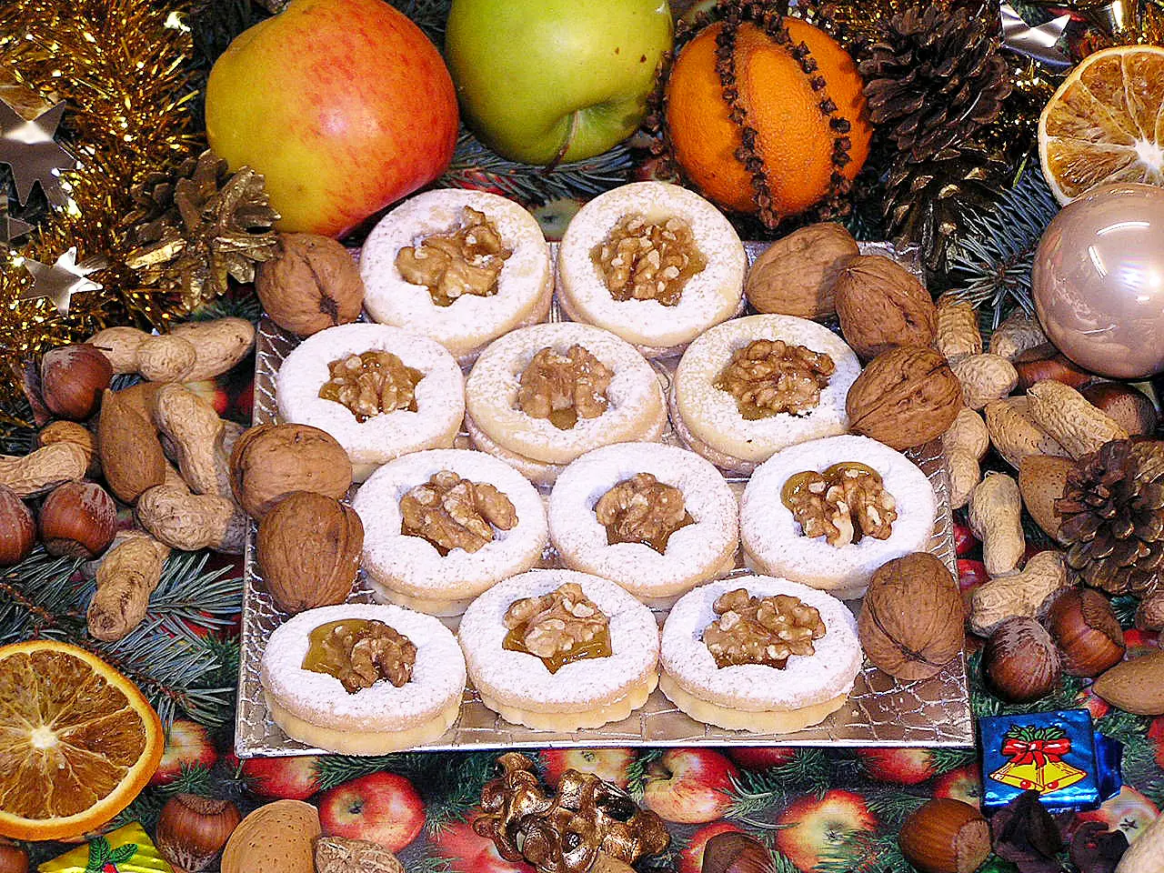 Walnuss-Spitz Gebäck mit Walnussfüllung auf weihnachtlich dekoriertem Untergrund mit Äpfeln und Nüssen