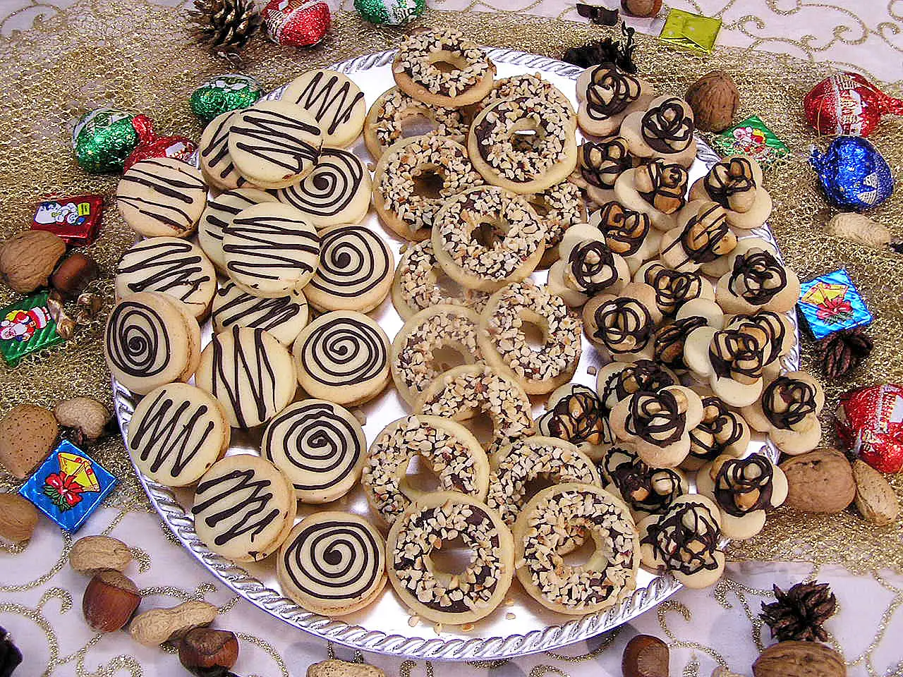 Nougat Taler und Nuss-Kringel mit Schokoladendekor auf weißer Platte, festlich arrangiert
