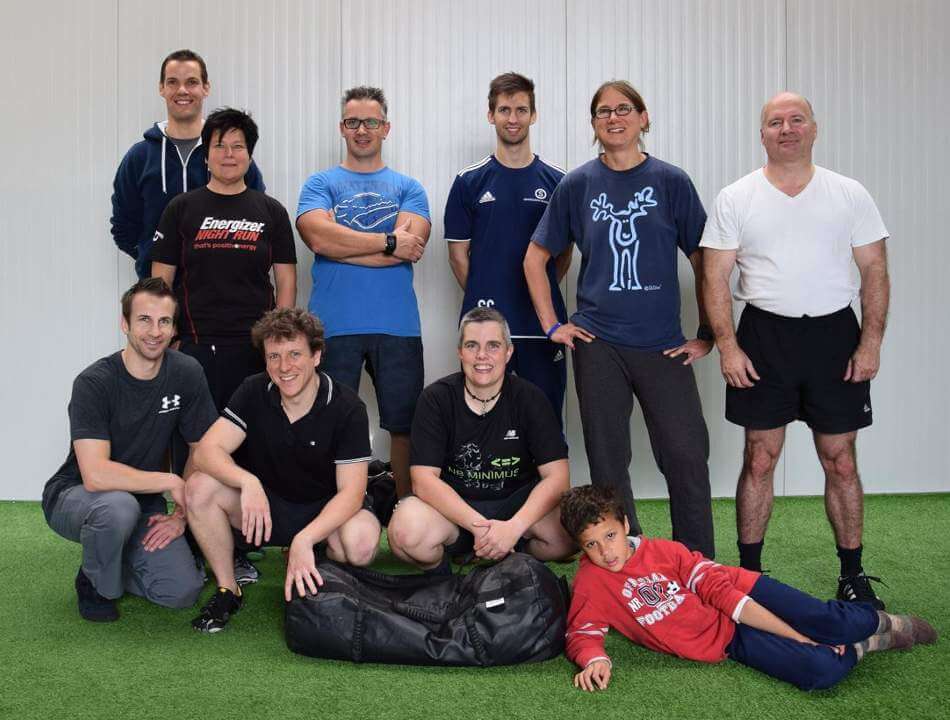 Gruppe von 9 Personen mit Sandsäcken auf Kunstrasenfläche, vielfältig gemischte Teilnehmer