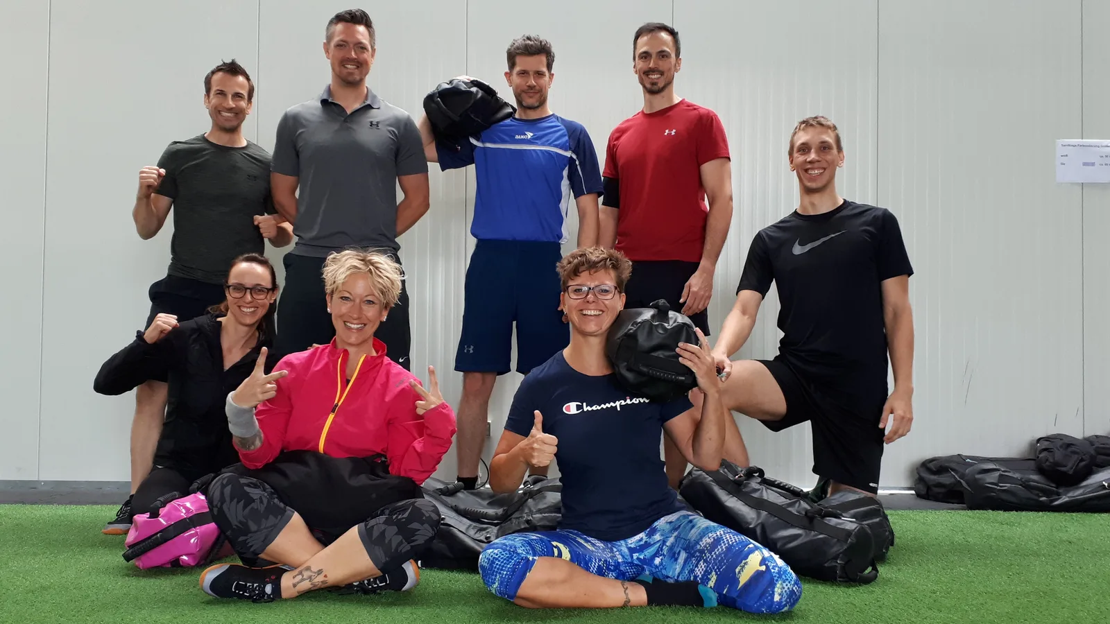 Gruppe von etwa 10 Personen mit Sandsäcken auf Kunstrasenfläche, freudige Atmosphäre