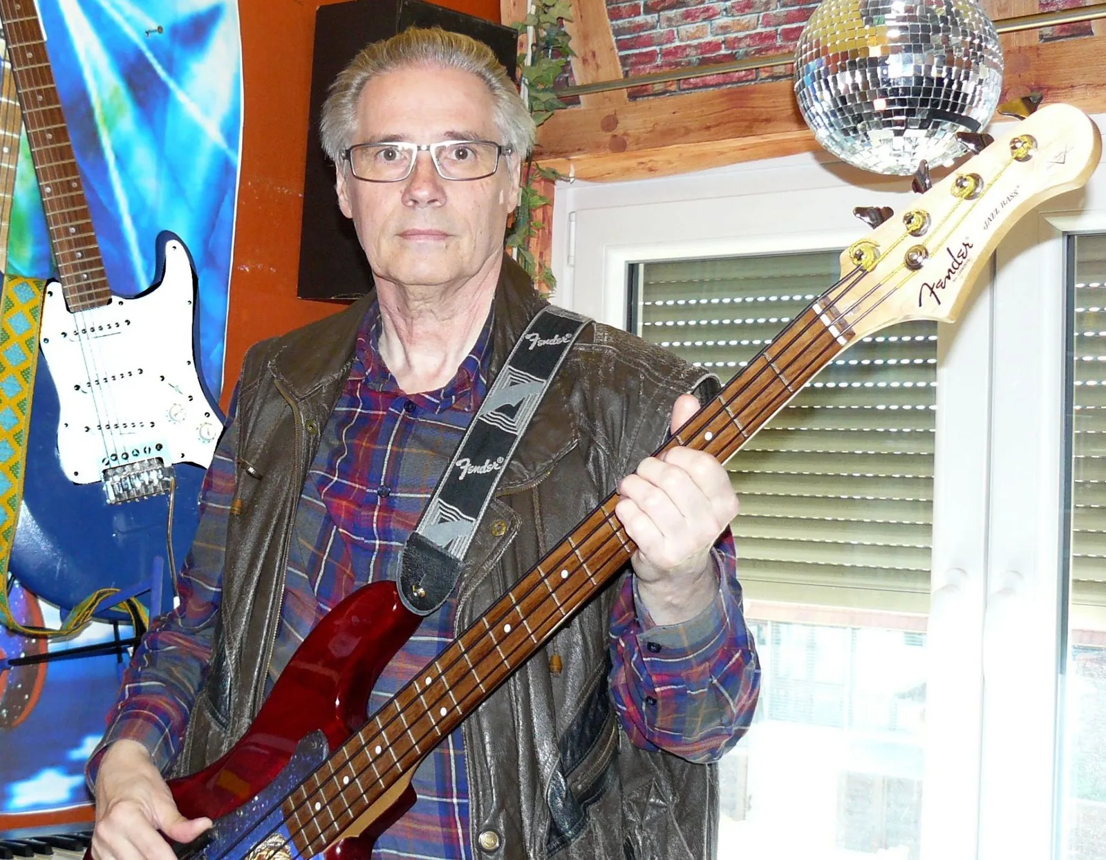 Dieter Bruchwalski hält rote Fender Precision Bass, trägt Lederjacke und Hemd, Musikstudio mit Discoball