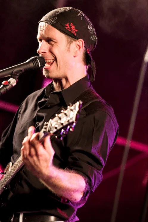 Andreas Vockrodt mit E-Gitarre bei Live-Auftritt, schwarzes Shirt mit Kopftuch, Bühnenlicht