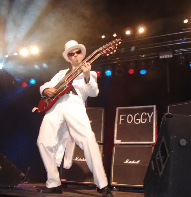 Musiker FOGGY in weißem Anzug und Hut mit rot-weißer E-Gitarre auf Bühne mit Marshallverstärker