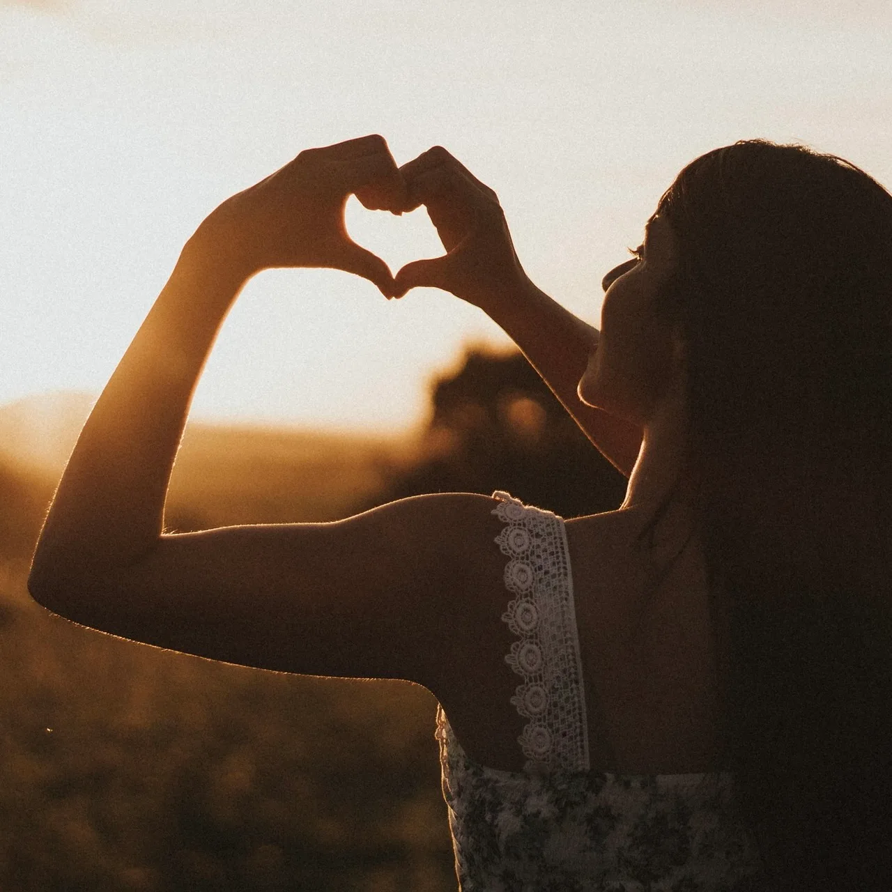 Echt-Gesund-Kongresspaket – Videokurs zu ganzheitl. Gesundheit 5 Frau macht Herzform mit Händen gegen Sonnenuntergang, Silhouette mit warmen Lichtern, Natur im Hintergrund