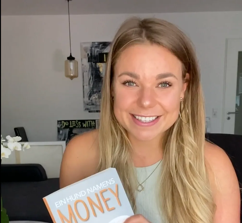 Porträt einer lächelnden Frau mit blonden Haaren, die das Buch "Ein Hund namens Money" hält