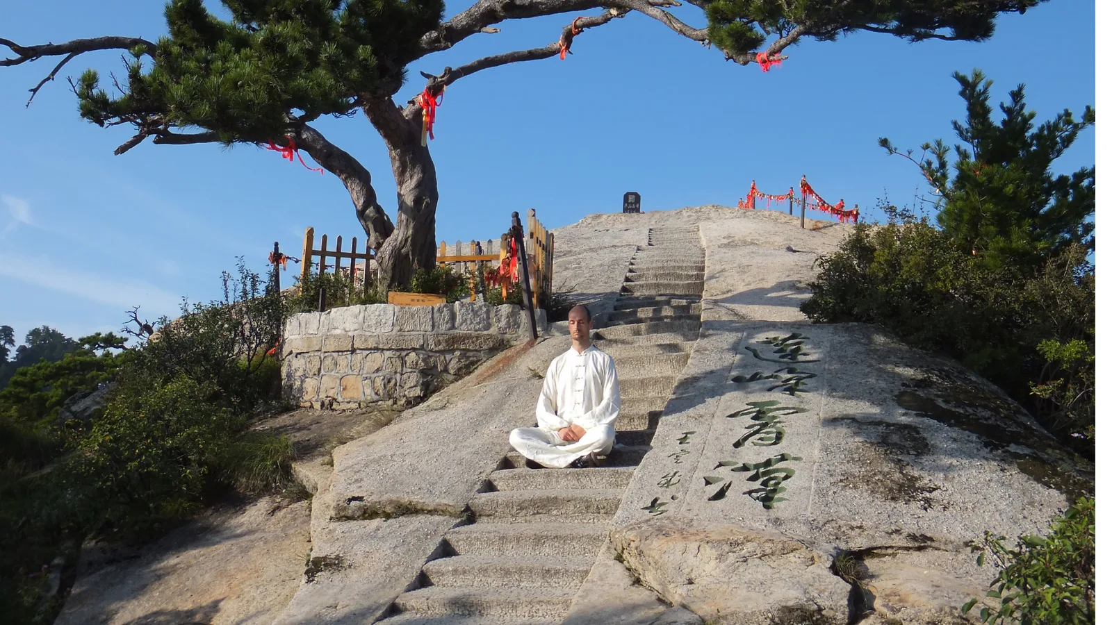 Tobias Puntke meditiert in weißem Leinengewand auf Steinstufen vor asiatischem Tempel mit roten Dekorationen