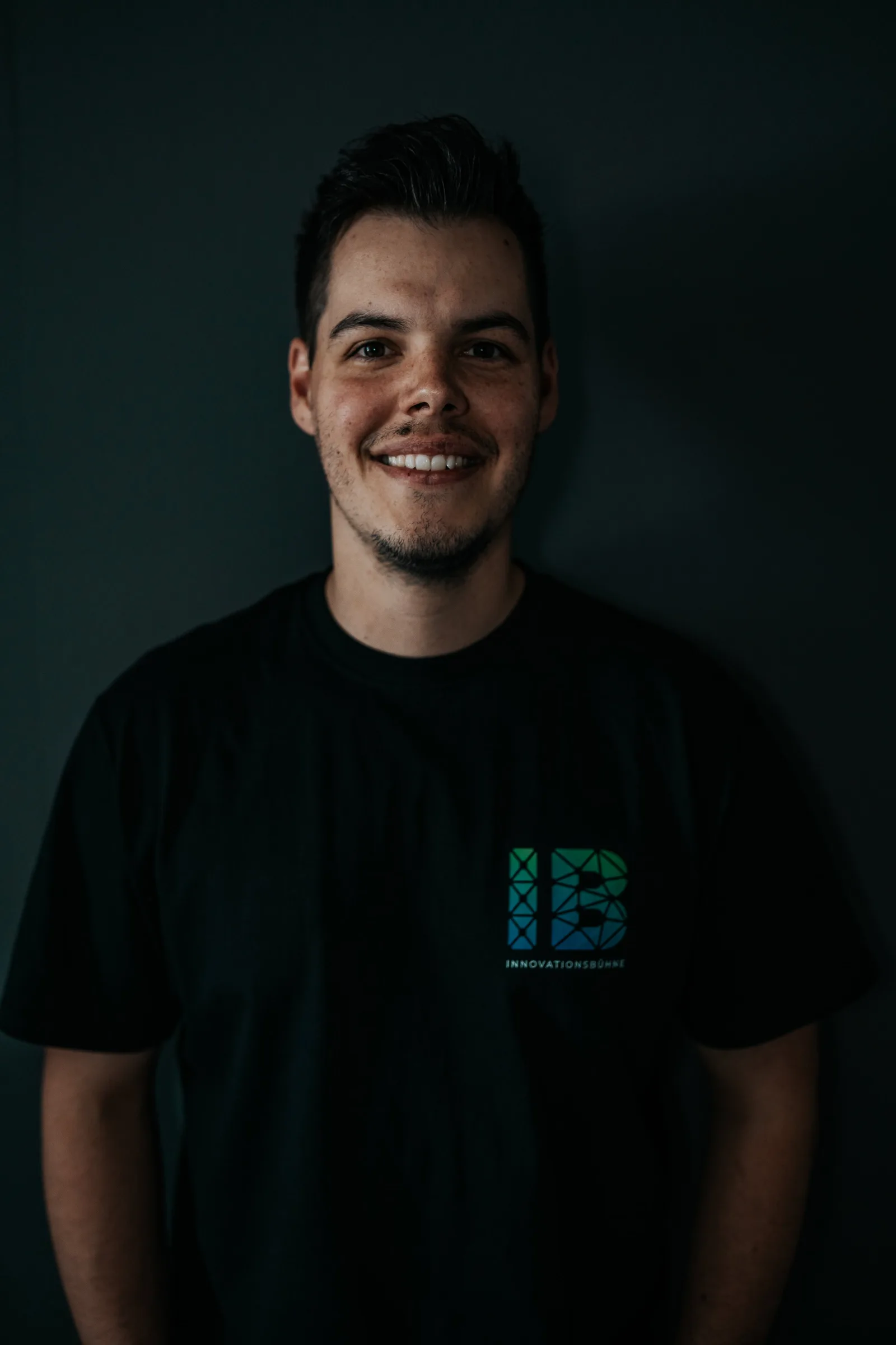 Einsteigerkurs Social Media & Reels von Vanessa Glaser 21 Porträt eines lächelnden Mannes in schwarzem Innovationsbühne-Shirt vor dunkelgrünem Hintergrund