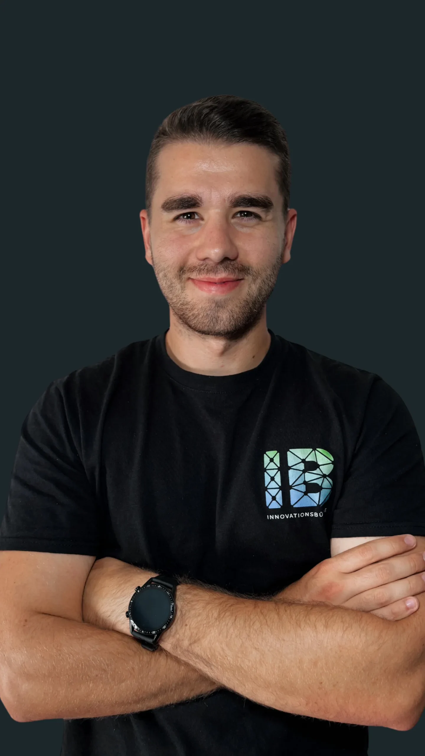 Einsteigerkurs Social Media & Reels von Vanessa Glaser 25 Porträtfoto eines Mannes mit schwarzem T-Shirt mit Innovationsbüro-Logo vor dunkelgrünem Hintergrund