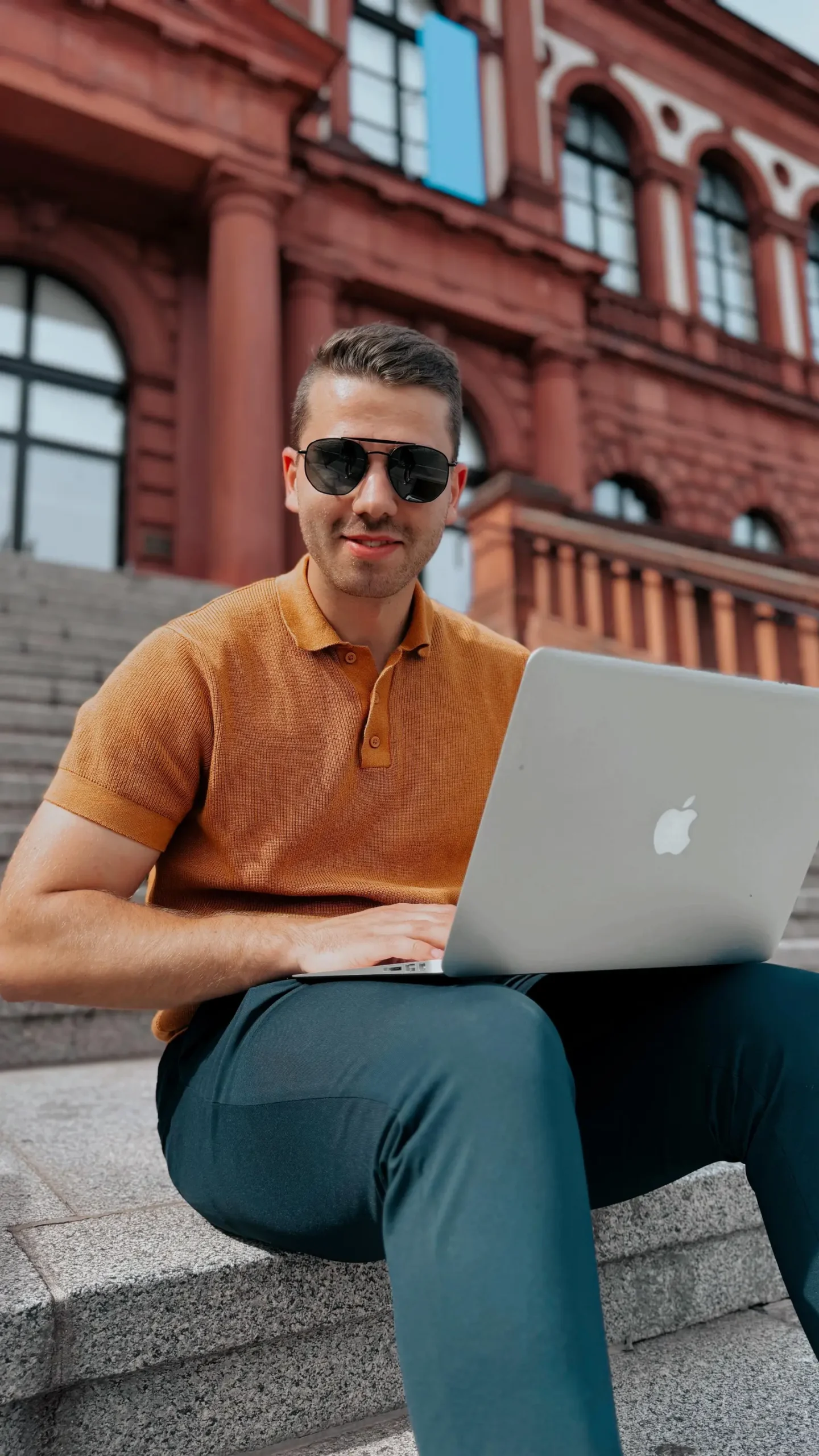 Einsteigerkurs Social Media & Reels von Vanessa Glaser 4 Mann mit Laptop auf Treppen vor Backsteingebäude, orange Poloshirt, Lifestyle-Fotografie