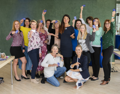 Gruppenfoto von etwa 15 Personen vor grüner Wand, viele halten blaue Flaschen hoch