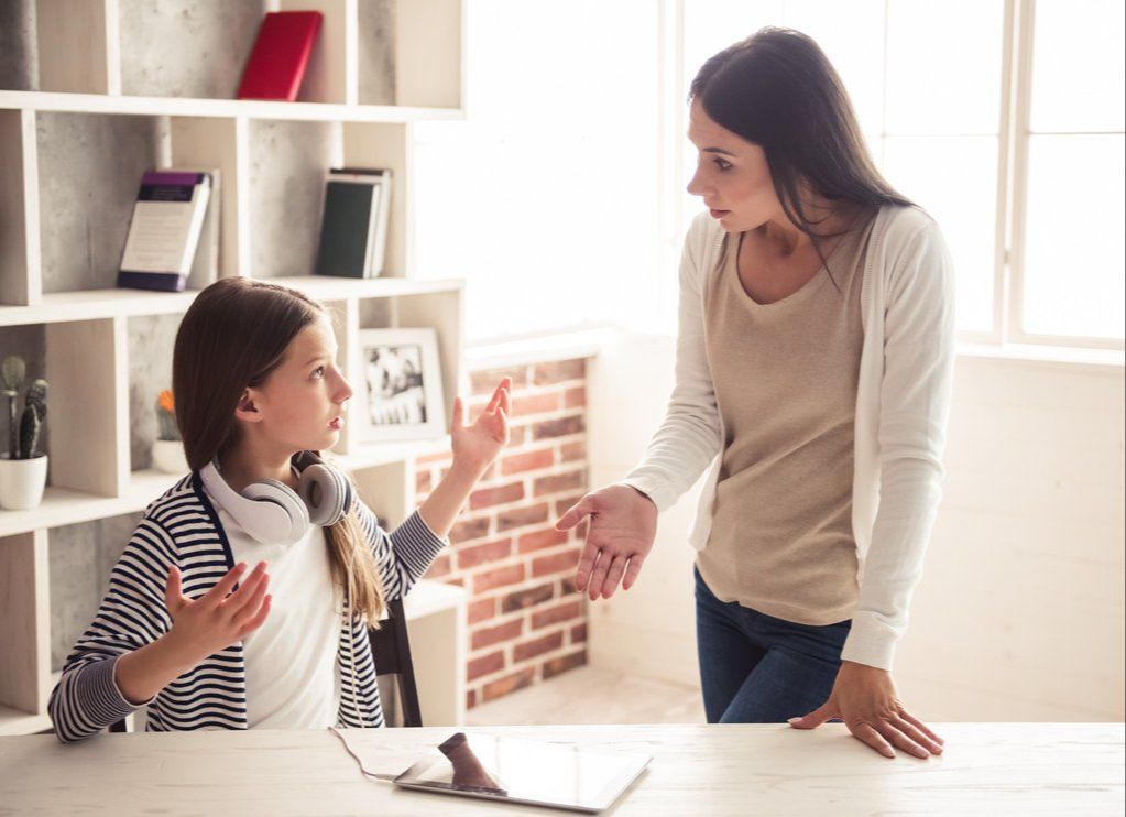 Mutter und Tochter im Gespräch am Tisch mit Tablet, helles Wohnzimmer mit Bücherregal