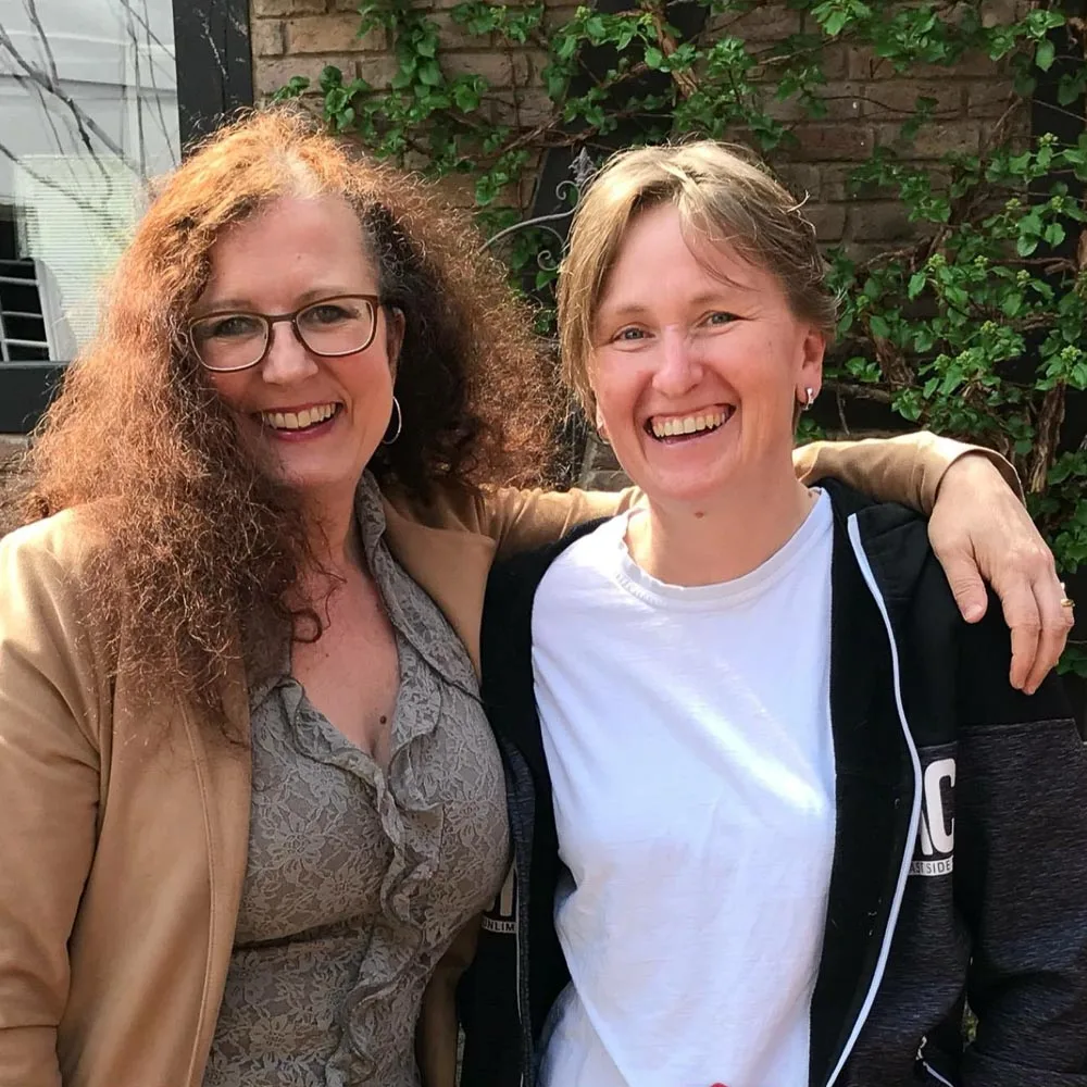 Zwei Frauen lachend vor Efeu – Sonja und Anja Team-Portrait